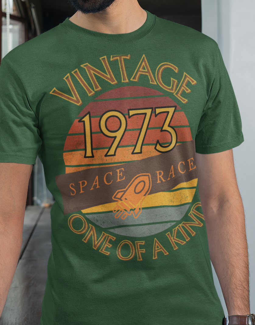 A man wearing a green T-Shirt with words vintage,1973,space race,one of a kind, image of a simple rocket in front of a brown distressed sunset
