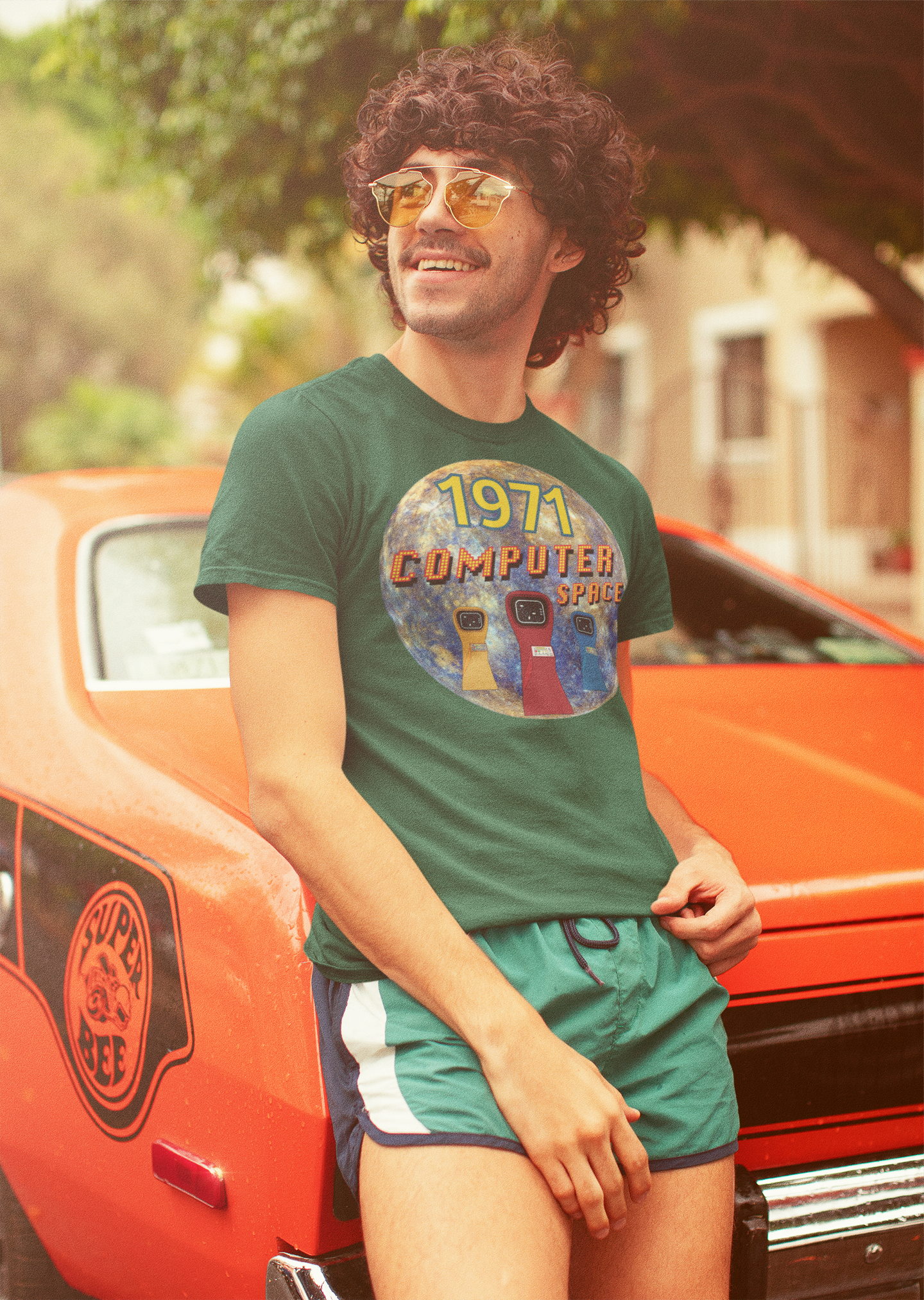 A man leaning on a classic car wearing a green T-Shirt with the words 1971,computer space,large earth, 3 computer space arcade game machines