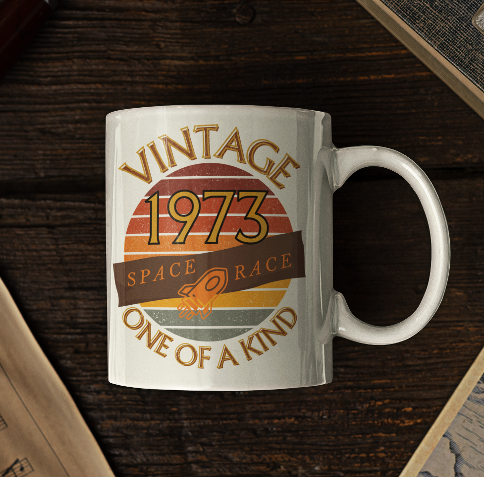White mug with words vintage,1973,space race,one of a kind, image of a simple rocket in front of a brown distressed sunset