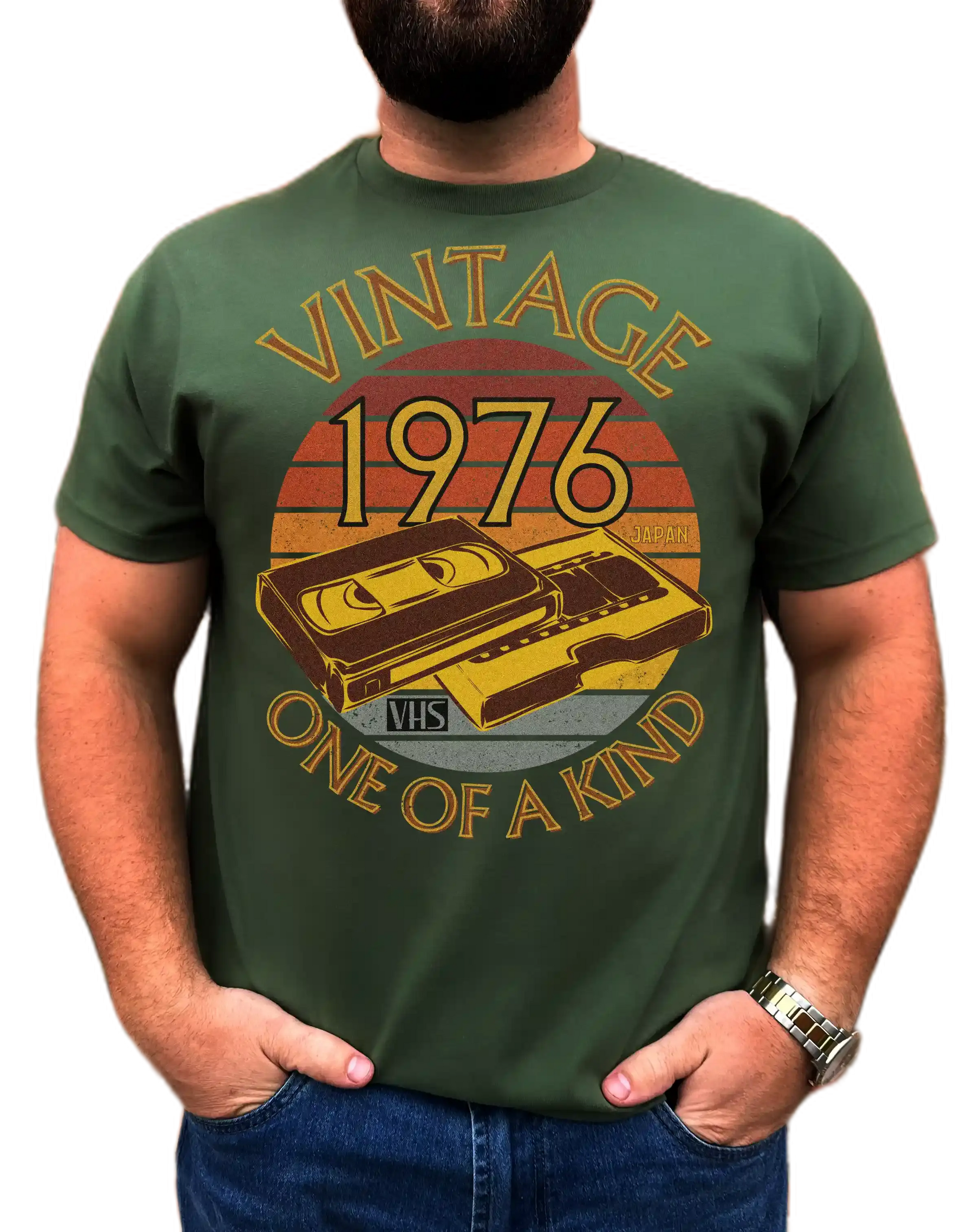 A man wearing a Green T-Shirt with words vintage,1976,japan,one of a kind, image of a simple VHS tape in front of a brown distressed sunset