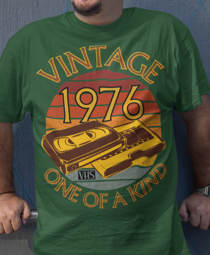 A man wearing a Green T-Shirt with words vintage,1976,japan,one of a kind, image of a simple VHS tape in front of a brown distressed sunset