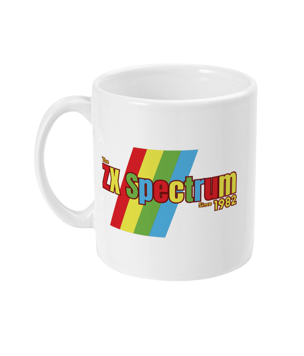 White mug featuring a retro design with the text "The ZX Spectrum" in bold, stylized font. The word "Spectrum" appears in a red-to-yellow gradient, with "Since 1982" in small yellow text below. Four diagonal rainbow stripes—red, yellow, blue, and light blue—run behind the text, referencing the iconic Sinclair ZX Spectrum branding. The shirt pays homage to the 1982 British home computer that sparked playground rivalries and a generation of 8-bit creativity.