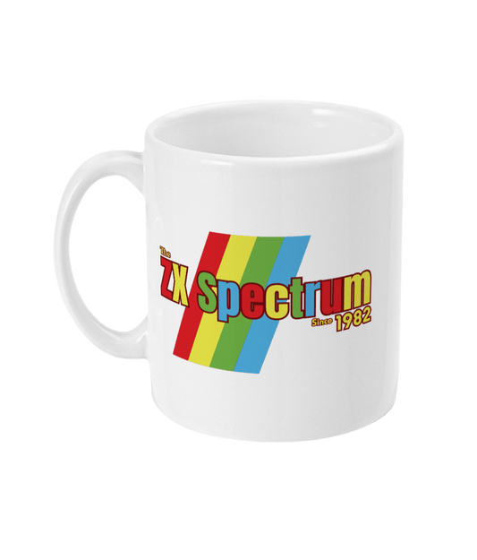 White mug featuring a retro design with the text "The ZX Spectrum" in bold, stylized font. The word "Spectrum" appears in a red-to-yellow gradient, with "Since 1982" in small yellow text below. Four diagonal rainbow stripes—red, yellow, blue, and light blue—run behind the text, referencing the iconic Sinclair ZX Spectrum branding. The shirt pays homage to the 1982 British home computer that sparked playground rivalries and a generation of 8-bit creativity.
