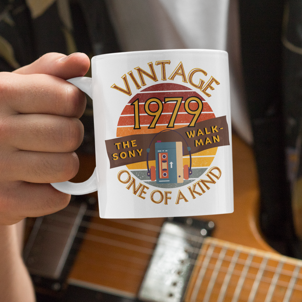 White mug  with words vintage,1979,the sony walkman,one of a kind, image of the original TPS-L2 model in front of a brown distressed sunset