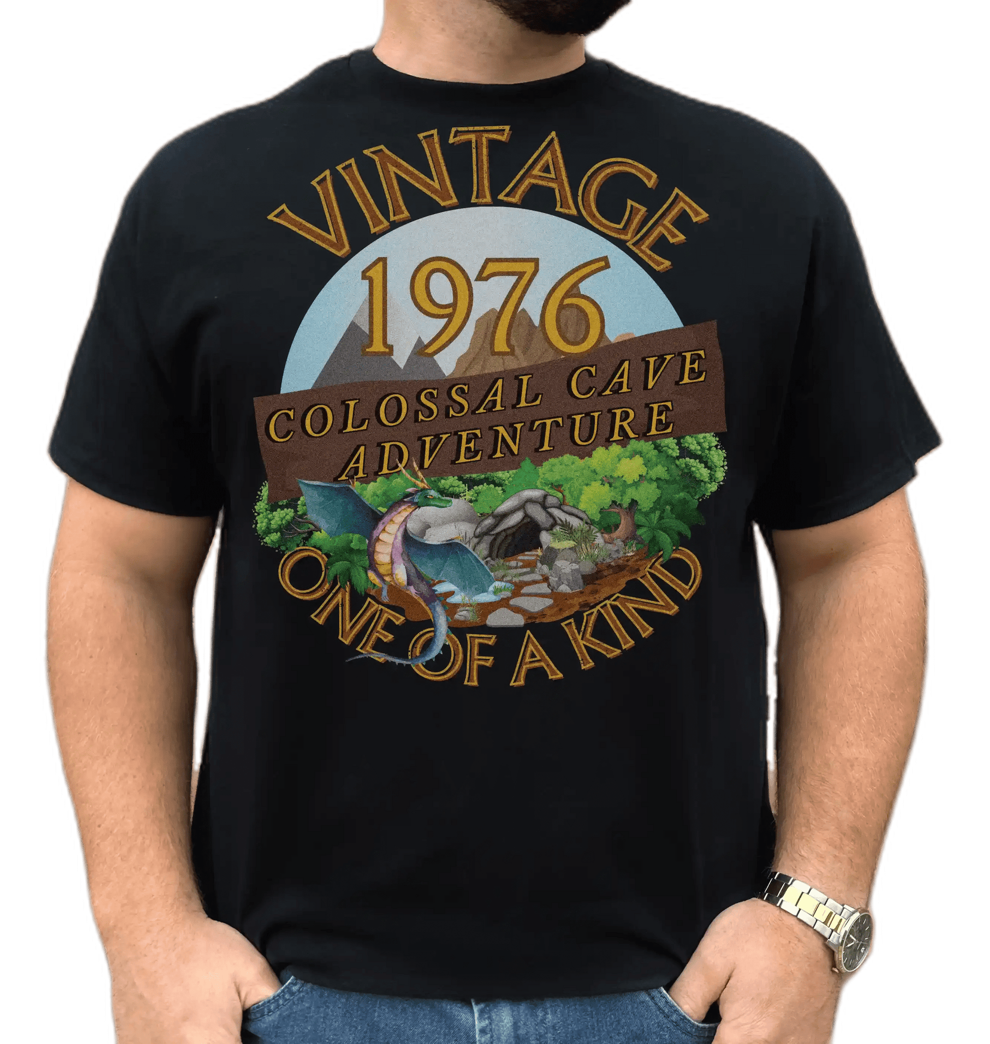 A man wearing a black T-Shirt with words vintage,1976,colossal cave adventure,one of a kind,circular picture of a dragon,cave and woodland,blue skyBlack T-Shirt with words,1976,colossal cave adventure,circular picture of a dragon,cave and woodland,blue sky,daytime