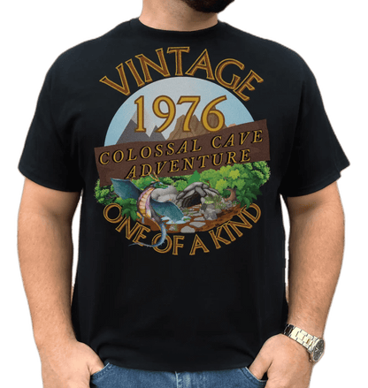 A man wearing a black T-Shirt with words vintage,1976,colossal cave adventure,one of a kind,circular picture of a dragon,cave and woodland,blue skyBlack T-Shirt with words,1976,colossal cave adventure,circular picture of a dragon,cave and woodland,blue sky,daytime