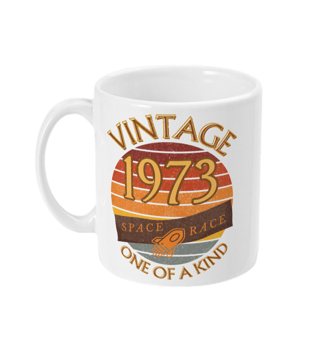 White mug with words vintage,1973,space race,one of a kind, image of a simple rocket in front of a brown distressed sunset