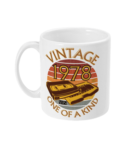 White mug mug with words vintage,1978,uk,one of a kind, image of a simple VHS tape in front of a brown distressed sunset